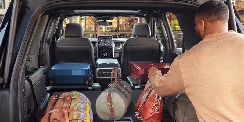 A person loads luggage into the spacious, open trunk of an SUV with folded-down back seats.