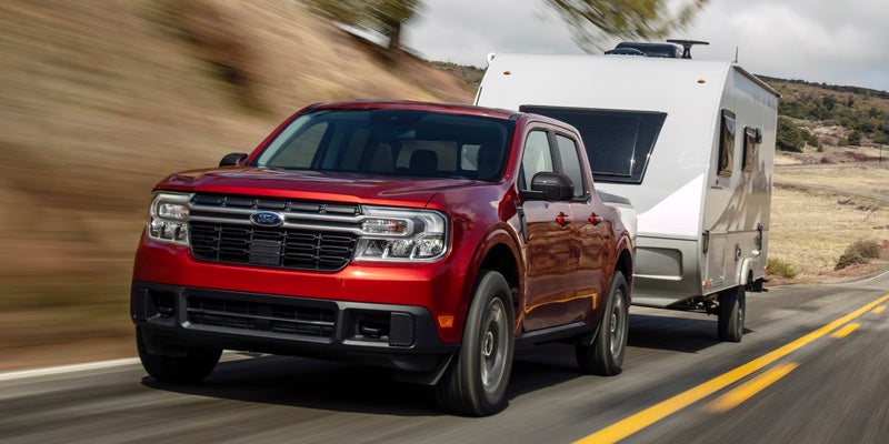 A red Ford Maverick truck tows a white camper trailer