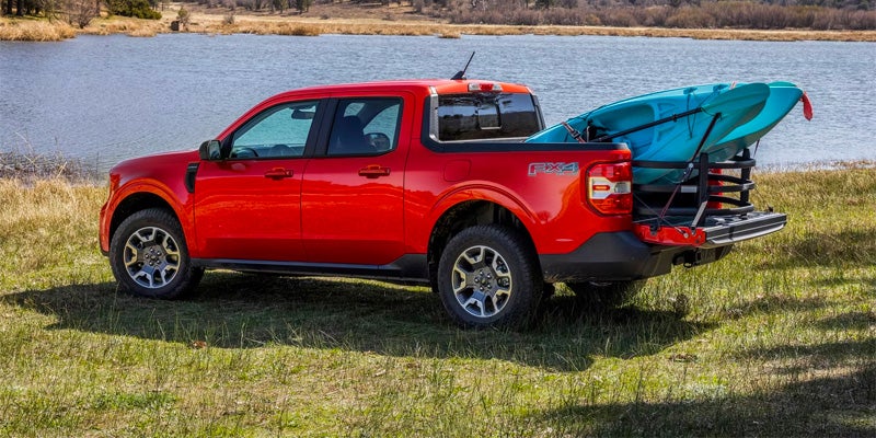 A red Ford truck carries two blue kayaks near water
