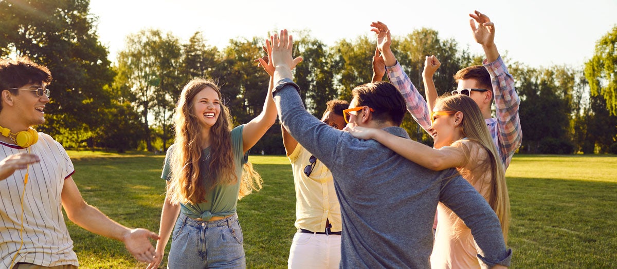 Diverse group of friends smiling and giving high-fives in a park