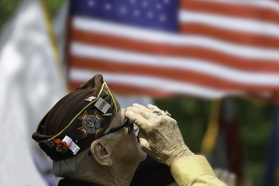 An elderly veteran in a VFW side cap salutes an American flag